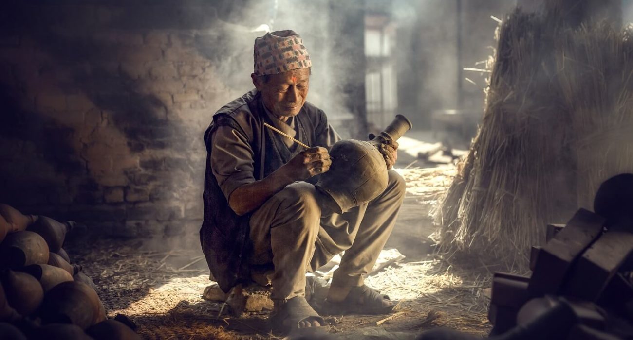 The old man is painting in a clay pot in Durbar square near old hindu temples.